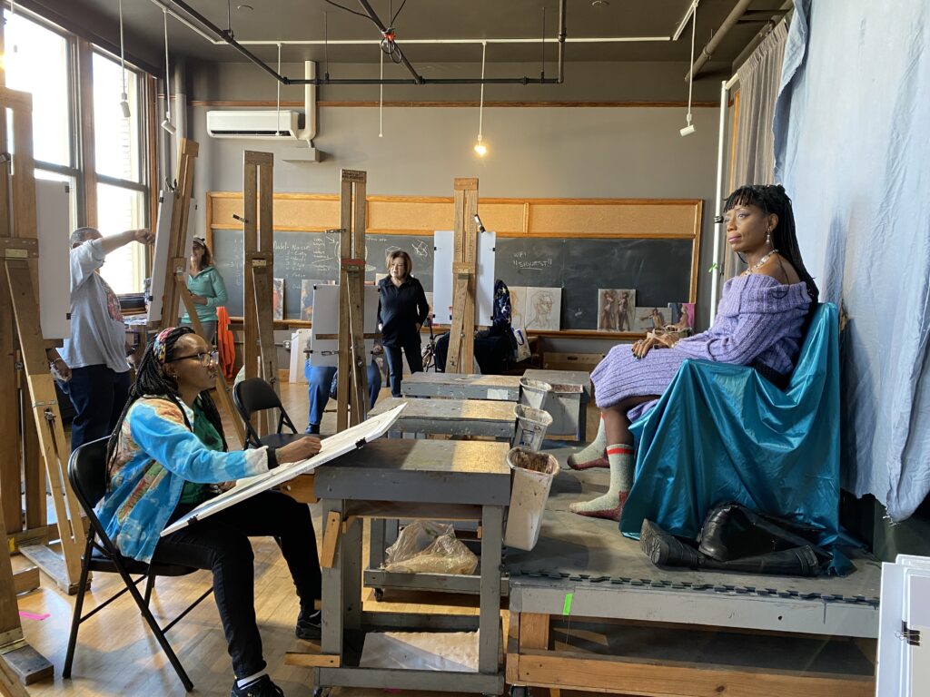 Photo of a student drawing from a live portrait model in a studio